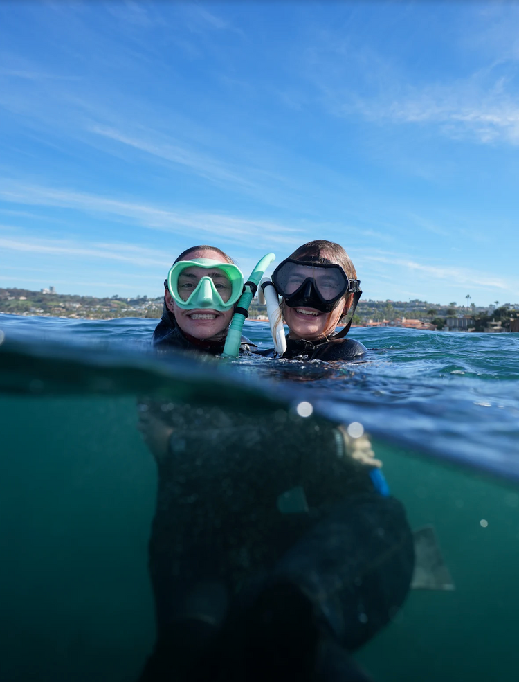 Two smiling divers in masks and snorkels floating at the surface off the San Diego coast
