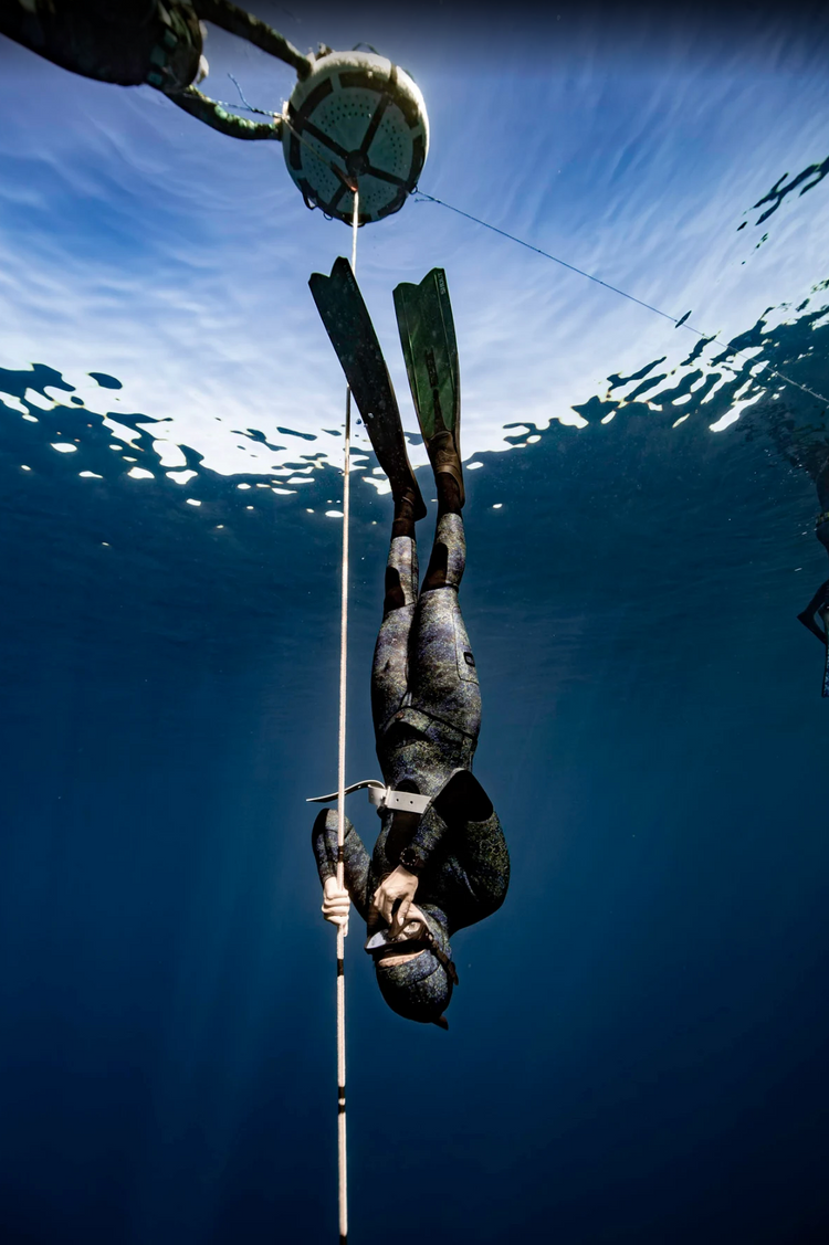 Freediver descending head-first along a dive line beneath a buoy in open water