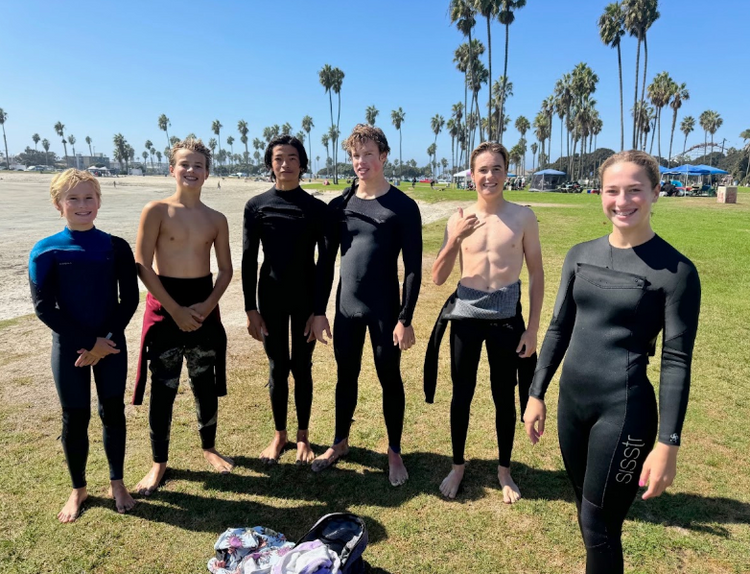 Group of smiling teen students in wetsuits on the grass by the beach after a youth freediving course